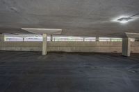 there is a empty parking garage with no cars parked on the pavement in it, and an empty parking area at one end