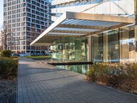 a modern glass building with an inner pond on a brick walk way near buildings and grass