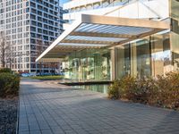 a modern glass building with an inner pond on a brick walk way near buildings and grass