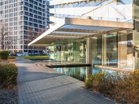 a modern glass building with an inner pond on a brick walk way near buildings and grass