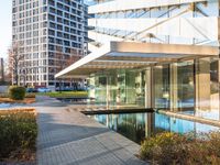 a modern glass building with an inner pond on a brick walk way near buildings and grass