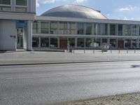 two people riding their bicycles past the building on the road, and pedestrians are outside