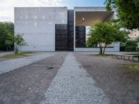 the paved path in front of the cement structure of the building is shaded by tree