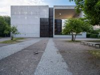 the paved path in front of the cement structure of the building is shaded by tree