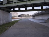 a paved pathway along a road below a bridge in a city with a river below