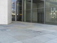 a person that is sitting on a skateboard on the ground near glass doors on the side of the building