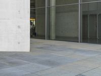 a person that is sitting on a skateboard on the ground near glass doors on the side of the building