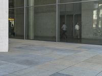 a person that is sitting on a skateboard on the ground near glass doors on the side of the building