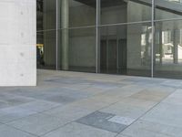 a person that is sitting on a skateboard on the ground near glass doors on the side of the building