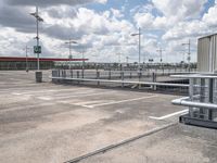 an empty parking lot with several large metal structures next to the sky and white clouds