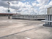 an empty parking lot with several large metal structures next to the sky and white clouds