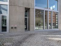 a person walking down the sidewalk of a building with several glass doors that open to reveal the courtyard below