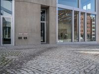 a person walking down the sidewalk of a building with several glass doors that open to reveal the courtyard below