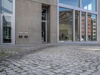 a person walking down the sidewalk of a building with several glass doors that open to reveal the courtyard below