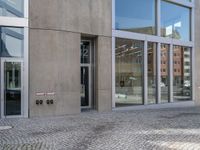 a person walking down the sidewalk of a building with several glass doors that open to reveal the courtyard below