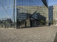 a person is taking their photograph in front of the glass walled building on a bricked street