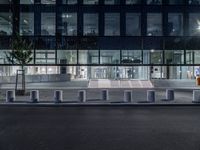 several concrete block benches and benches along a street at night near a building, there is lit up windows with reflective light