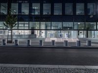 several concrete block benches and benches along a street at night near a building, there is lit up windows with reflective light