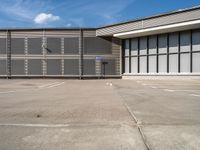 an empty parking lot has a no parking sign on the side of it and a large warehouse in the background