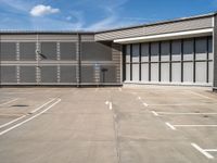 an empty parking lot has a no parking sign on the side of it and a large warehouse in the background