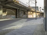 a empty roadway under a bridge next to an overpass and several buildings with graffiti