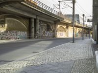 a empty roadway under a bridge next to an overpass and several buildings with graffiti