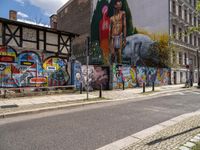 a wall with different colorful artwork on it in a city with buildings around and the street has a bike path going under it