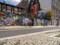 a wall with different colorful artwork on it in a city with buildings around and the street has a bike path going under it