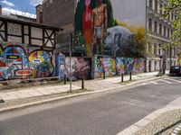 a wall with different colorful artwork on it in a city with buildings around and the street has a bike path going under it