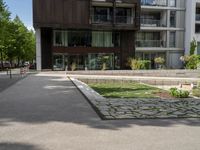 a paved walkway leading to a brown apartment building, on a sunny day with a red sign beside a park