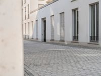 an empty sidewalk in front of some white buildings on a sunny day, looking at the street