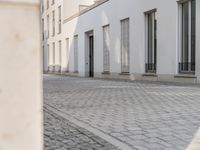 an empty sidewalk in front of some white buildings on a sunny day, looking at the street