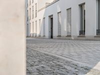 an empty sidewalk in front of some white buildings on a sunny day, looking at the street