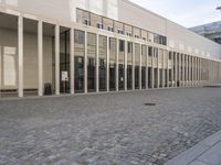 large building that has several tall glass windows on the side of it and brick driveway beside it