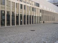 large building that has several tall glass windows on the side of it and brick driveway beside it