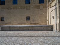 the sidewalk is paved with stones and has a bench in front of it, with no people inside