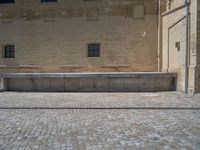 the sidewalk is paved with stones and has a bench in front of it, with no people inside