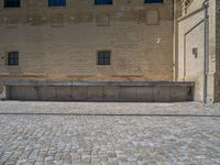 the sidewalk is paved with stones and has a bench in front of it, with no people inside