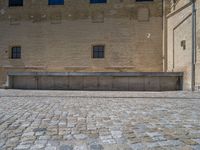 the sidewalk is paved with stones and has a bench in front of it, with no people inside