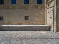 the sidewalk is paved with stones and has a bench in front of it, with no people inside