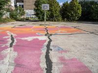 painted graffiti marks in an empty parking lot with a basketball court on the ground and a street sign to the left