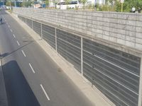 a wall made of concrete next to highway with cars on it and trees near side of road