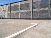 an empty basketball court and a tall steel building with several rows of sliding gates on it