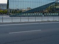 a street next to a modern glass building with a curved exterior and railings on the sides