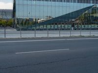 a street next to a modern glass building with a curved exterior and railings on the sides