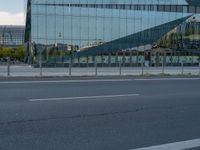 a street next to a modern glass building with a curved exterior and railings on the sides