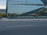 a street next to a modern glass building with a curved exterior and railings on the sides