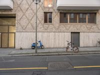 three bikes leaning against a pole by a building with windows and doors in front of it