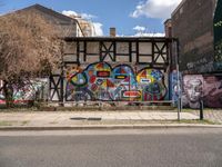 a wall with different colorful artwork on it in a city with buildings around and the street has a bike path going under it