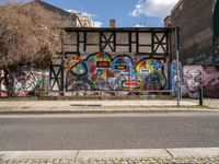 a wall with different colorful artwork on it in a city with buildings around and the street has a bike path going under it